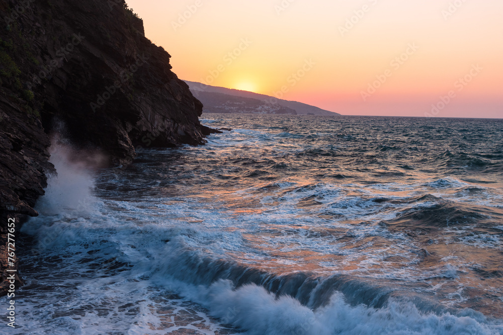 Scenic view to the costal town of Evdilos with rough sea and rocky coast at sunset.