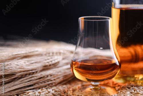 A glass of whiskey with bottle and barley ears on barley grains as background. Whiskey distillery concept