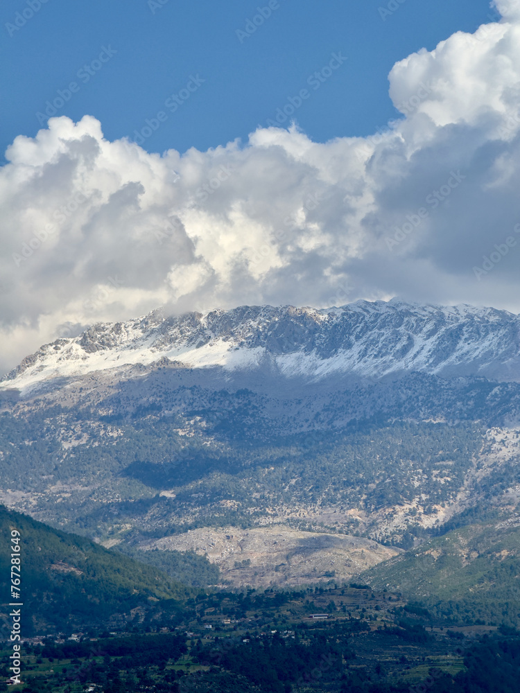 Snow-capped mountain peaks rise majestically above the lush landscape near Köprülü Canyon, framed by billowing clouds. Snow-capped mountain peaks rise majestically above the lush landscape near Köprülü Canyon, framed by billowing clouds.