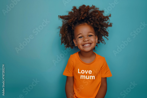 Photo portrait of a smiling African American kid wearing a t-shirt with a phrase Love mum, standing against the blue wall, vibrant bold design photo