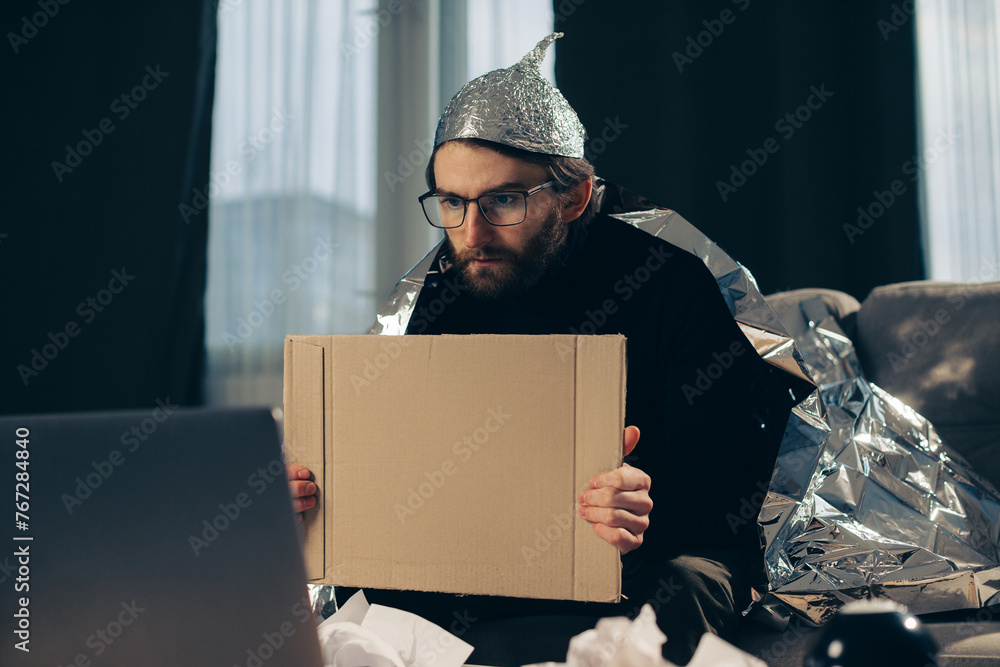 A conspiracy theorist in a tinfoil hat holds a sign in his hands. - obrazy, fototapety, plakaty 