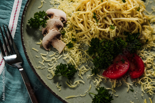 noodles spagetti, pasta with butter served with tomatoes, mushrooms and green parsley on textile mediterranean colors table cloth, blue napkin and dry palm leaves photo