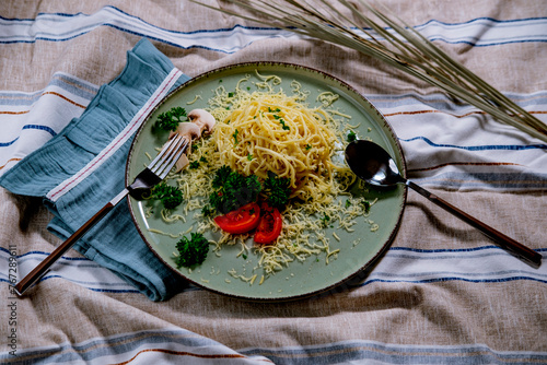 noodles spagetti with butter served with cheese, tomatoes , mushroom and parsley on table cloth, blue napkin, light green ceramic plate photo