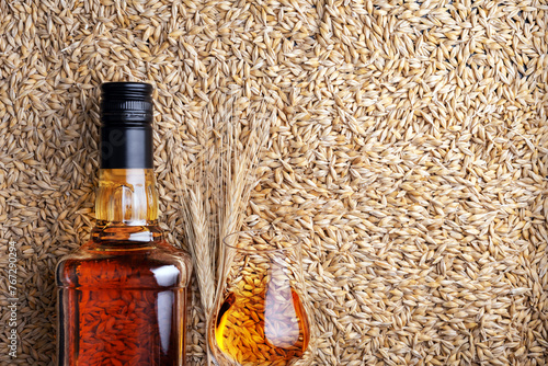 A glass of whiskey with bottle on barley grains as background, top view