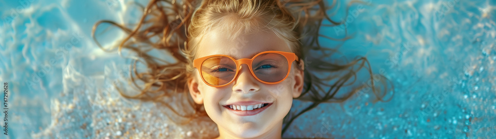 Portrait of a beautiful cheerful child, a 12-year-old girl in sunglasses, lies in the water on the shore. Top view. Banner. Portrait of a beautiful cheerful child, a 12-year-old girl in sunglasses, lies in the water on the shore. Top view. Banner.