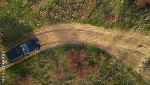 Aerial high angle top down shot of a black car towing a small trailer with two off road cross morotbikes along a windy dirt road. Drone footage of vehicle with a trailer behind going to sports event.
 photo