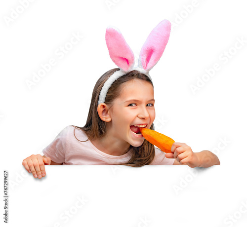 Funny little girl wearing bunny ears with a carrot in her hand. The child eats a carrot. Isolated on a white background.