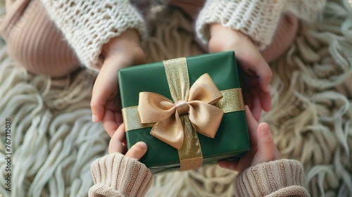 closeup of kids hands holding green gift box with gold ribbon, perfect present for Christmas, New Year, or Three Kings Day celebration photo