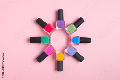 Coloured bright nail polish bottles stacked circle on a pink background