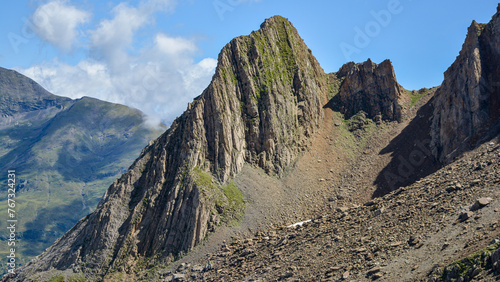 A beautiful peak in French Pyrenees, red colour with greenery, blue sky with some clouds