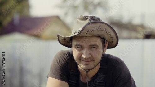 A man takes a break from preparing the soil with a cultivator in the backyard. Portrait of a male Farmer in a hat with a walk-behind tractor in the backyard of a vegetable garden