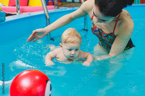 A 6-month-old baby learns to swim with a coach in the pool. Swimming pool for babies. Children's development