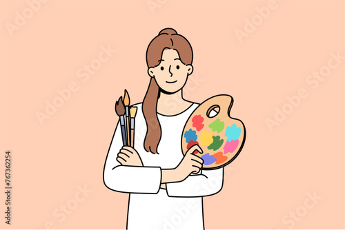 Woman artist holds brushes for painting and palette for mixing watercolor paints. Portrait of beautiful artist girl who is interested in creative hobby and wants to exhibit in art gallery