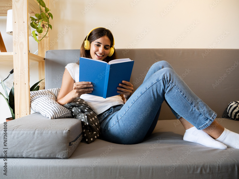 Carefree young woman reading a book on the sofa in an apartment. Literature and reading Carefree young woman reading a book on the sofa in an apartment. Literature and reading