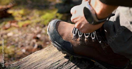 man tying hiking boot shoelace on fallen tree trunk. outdoor footwear and clothing photo