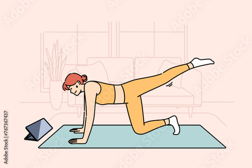 Woman doing fitness watching online lesson from trainer, doing stretching on sports mat in living room. Girl is interested in fitness and health-improving gymnastics, thanks to webinars from internet.