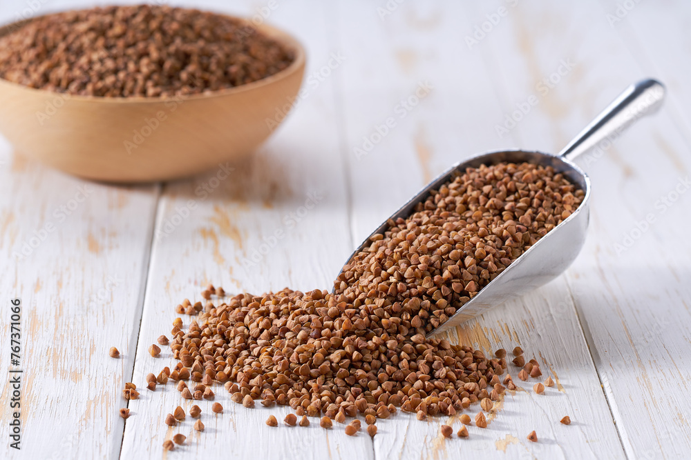 Raw buckwheat in a metal scoop on a white wooden table. Raw buckwheat in a metal scoop on a white wooden table.