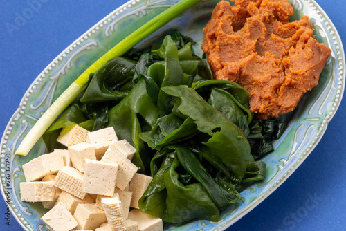 Cubed tofu, rehydrated wakame seaweed, red miso paste, and scalion. Main ingredients for many asian dishes. Blue background. photo