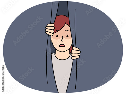 Scared girl peeping behind curtain