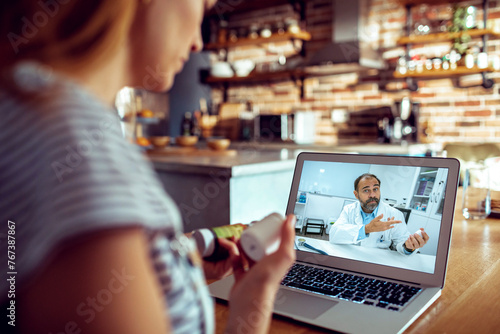 Woman holding pill bottle having video call with doctor at home photo