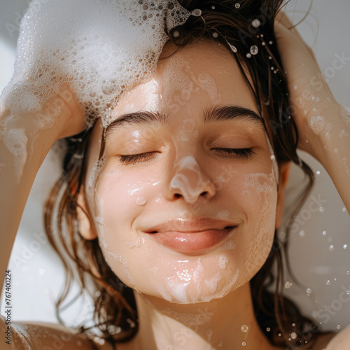 A close-up of a woman washing her hair, a lot of foam on her hair and face, and she is smiling.