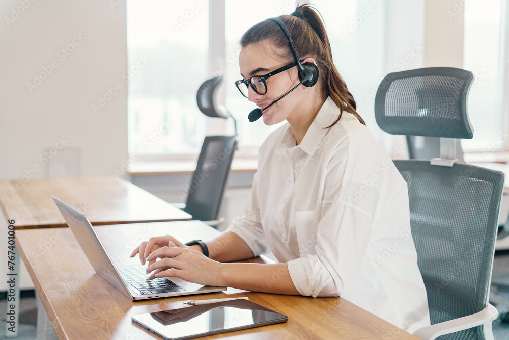 Captured in mid-conversation, a professional operator is a female dispatcher with a headset types on a laptop in a bright office, illustrating a dynamic work environment. Captured in mid-conversation, a professional operator is a female dispatcher with a headset types on a laptop in a bright office, illustrating a dynamic work environment.