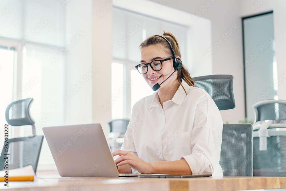 A smiling customer service representative with a headset works diligently on a laptop in a bright, contemporary office setting. A smiling customer service representative with a headset works diligently on a laptop in a bright, contemporary office setting.