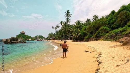 A man walking on the sand in a paradisiacal beach with palms and turquoise water, in the tayrona national park in colombia photo