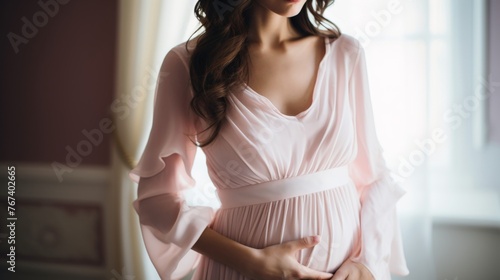 Pretty pregnant woman in soft pink textile clothes showing off her pregnancy belly