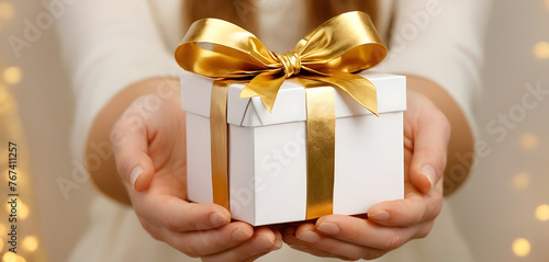 Woman hands holding wrapped white box with golden bow, focus on box mothers day concept 