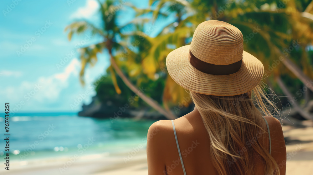 Rear view of a young woman in hat on the tropical beach with palm trees and blue ocean or sea with space for copy