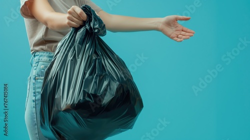 Closeup woman hand throwing away black polyethylene garbage bag on isolated blue background with space for copy photo