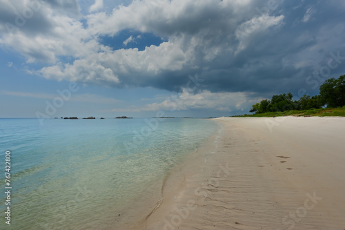 Nice white sand beach with calm turquoise  blue w  ter surrounded by green vegetation with black cloud in Pantai Mabai  Belitung  Sumatera  Indonesia