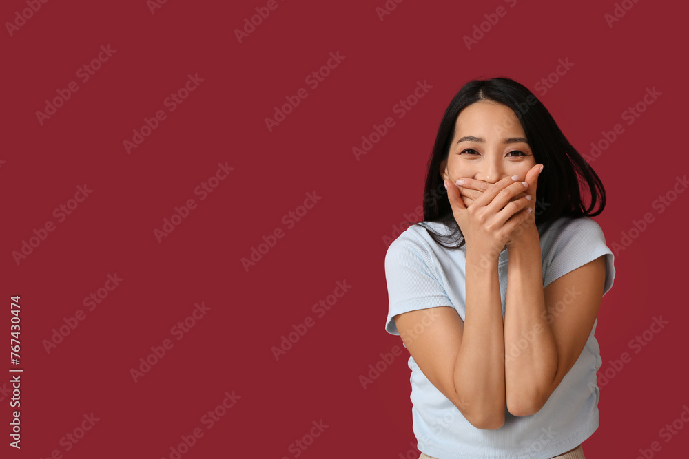 Young Asian woman laughing on red background