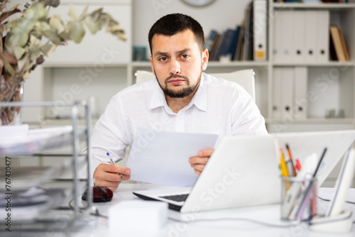 Serious male office worker sitting at desk and doing paperwork.