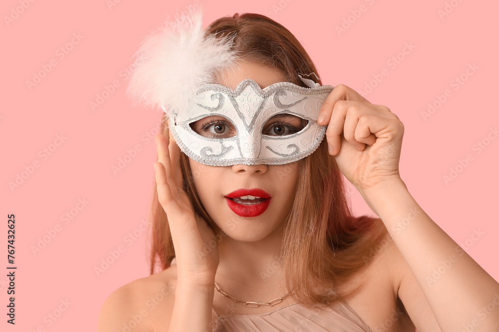 Beautiful young woman in white carnival mask on pink background
