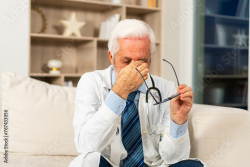 Sad tired mature senior male doctor in medical uniform in hospital or doctor office. Unhappy General Practitioner GP therapist professional healthcare expert in clinic. Healthcare concept