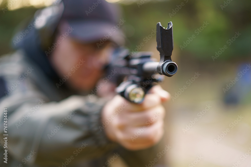 A man is holding a gun with a black flag on it. The man is wearing a green jacket and a black hat A man is holding a gun with a black flag on it. The man is wearing a green jacket and a black hat