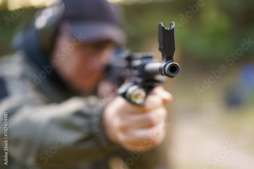 A man is holding a gun with a black flag on it. The man is wearing a green jacket and a black hat