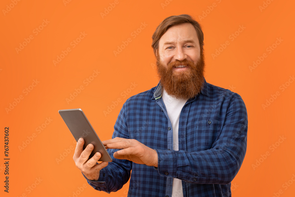 Redhaired bearded businessman using digital tablet on orange backdrop Redhaired bearded businessman using digital tablet on orange backdrop