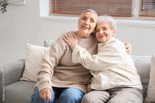 Senior female friends hugging on sofa at home