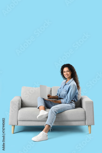 Free Download Young African-American woman using laptop on sofa against blue background - GFXLoad