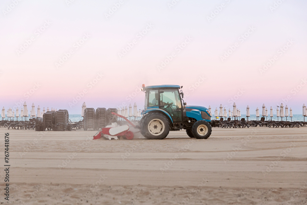 Obraz premium Tractor smoothes the sand on public beach by the sea