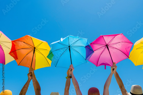 a group of friends' hands raising colorful beach umbrellas against a backdrop of clear blue skies, marking their spot on the sandy shores for a day of fun and relaxation in the sun
