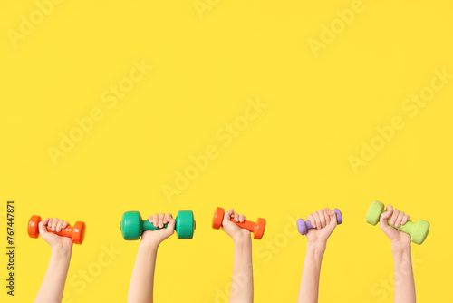 Female hands with different dumbbells on yellow background