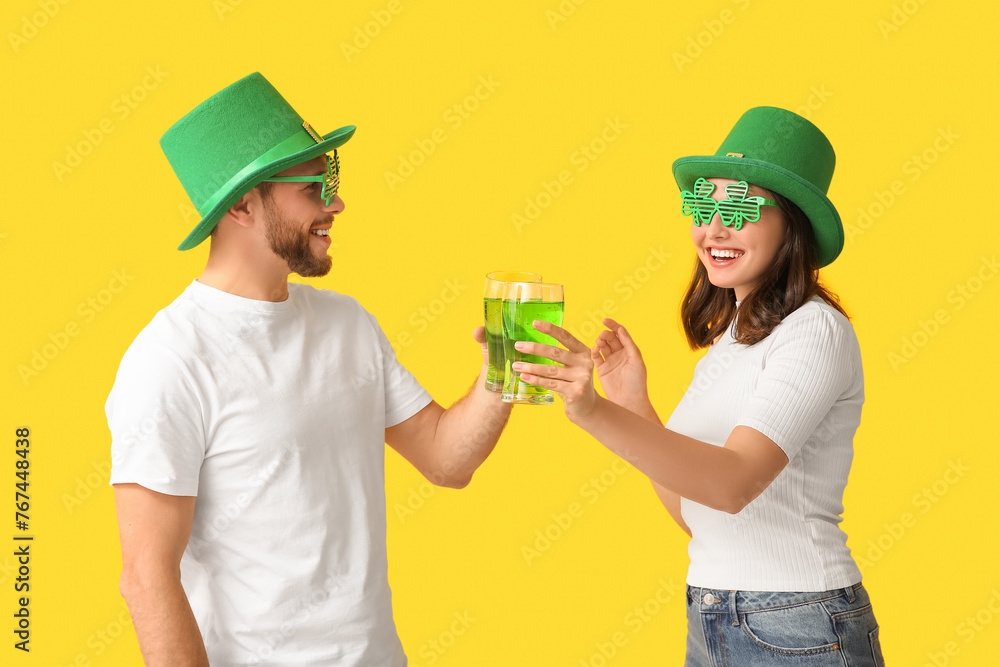 Beautiful young couple in leprechaun hats with glasses of beer on yellow background. St. Patrick's Day celebration Beautiful young couple in leprechaun hats with glasses of beer on yellow background. St. Patrick's Day celebration