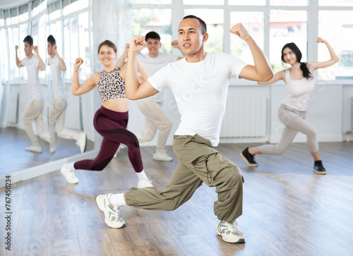Positive smiling young man dancing hip hop with group of guys and girls in modern dance class