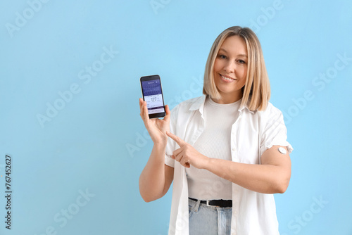 Diabetic woman with glucose sensor using mobile phone for measuring blood sugar level on blue background