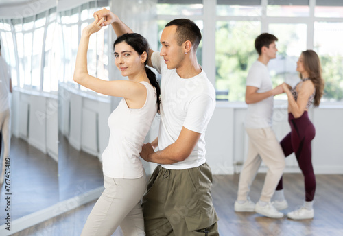 Happy young woman enjoying training dancing active swing with male partner in modern dance room. Social dancing concept