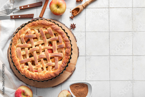 Tasty homemade apple pie with fruits, cinnamon and cutlery on white tile background photo